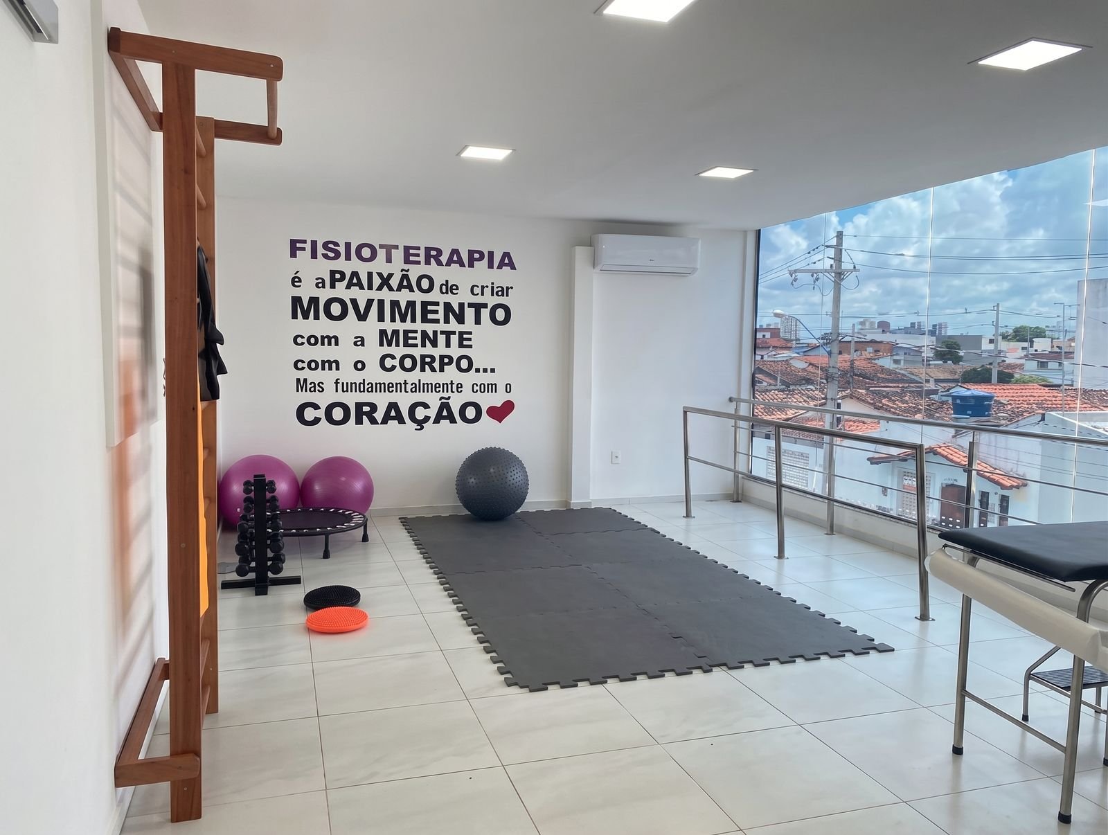 Sala de fisioterapia com espaldar, bolas, colchonete e janela de vidro